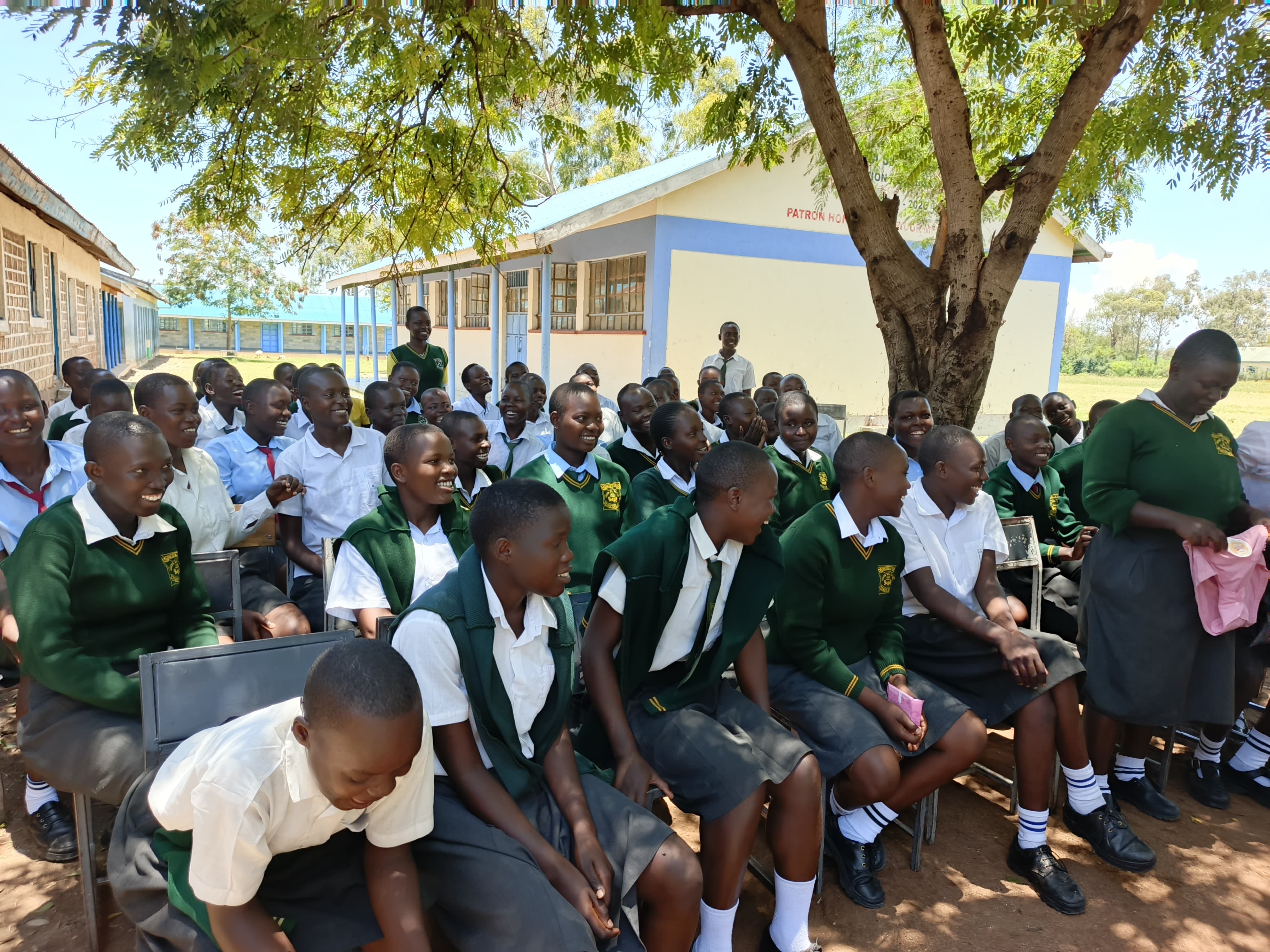 Community members gathered together for a meeting under a tree in a rural Kenyan village.